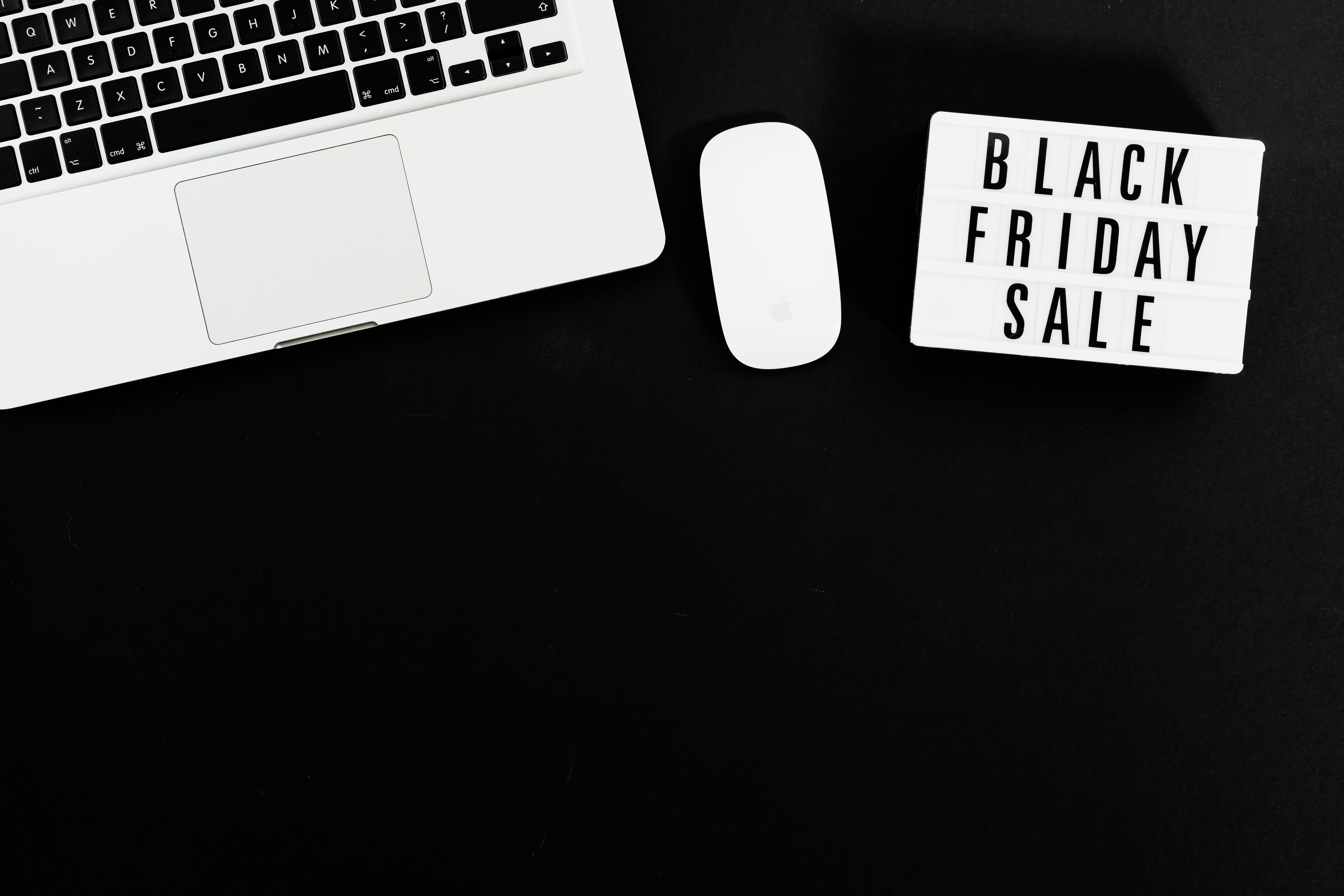 White laptop keyboard and white wireless mouse on a black surface next to a lightbox sign reading Black Friday Sale